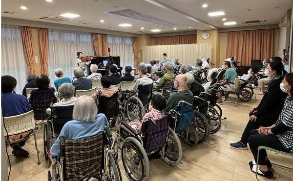 高齢者施設で、ヴァイオリンとピアノの演奏に耳を傾ける利用者の方々